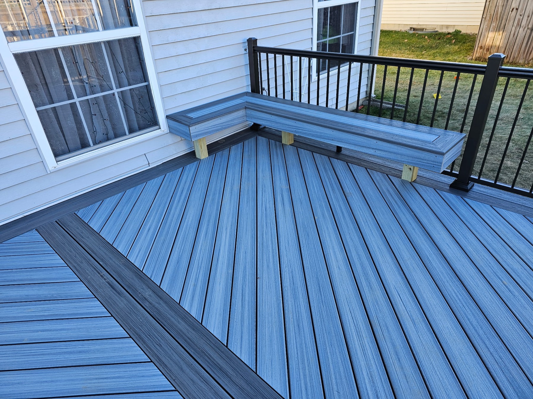 Grey composite deck boards laid diagonally inside a charcoal border, with a built-in L-shaped bench and black railing
