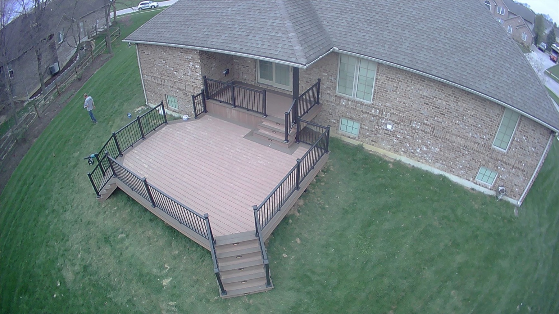 Aerial view of a raised composite deck with black railing, two stairways and steps up to a covered back door