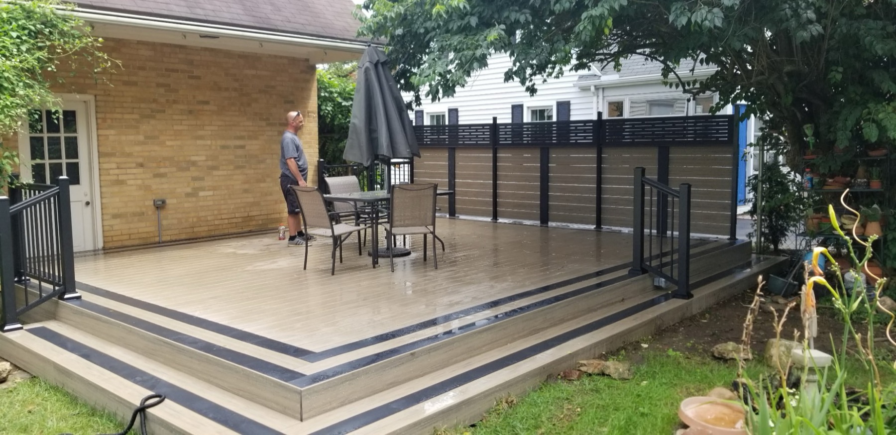Light composite deck with charcoal-striped steps, black railing and a composite privacy screen wall along one side