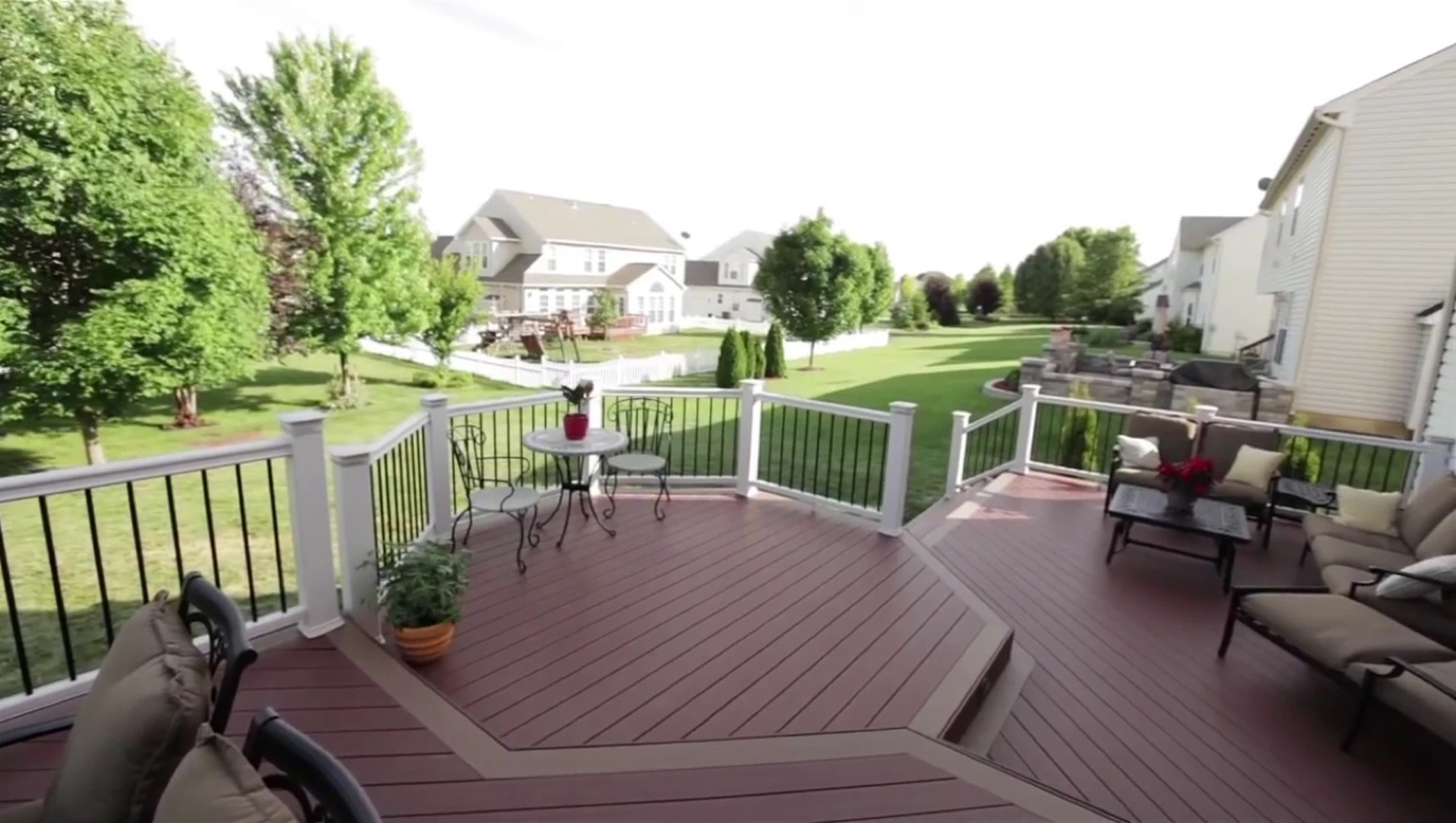 Red-brown composite deck with diagonal boards, a step-down lounge area, white rail posts and black balusters