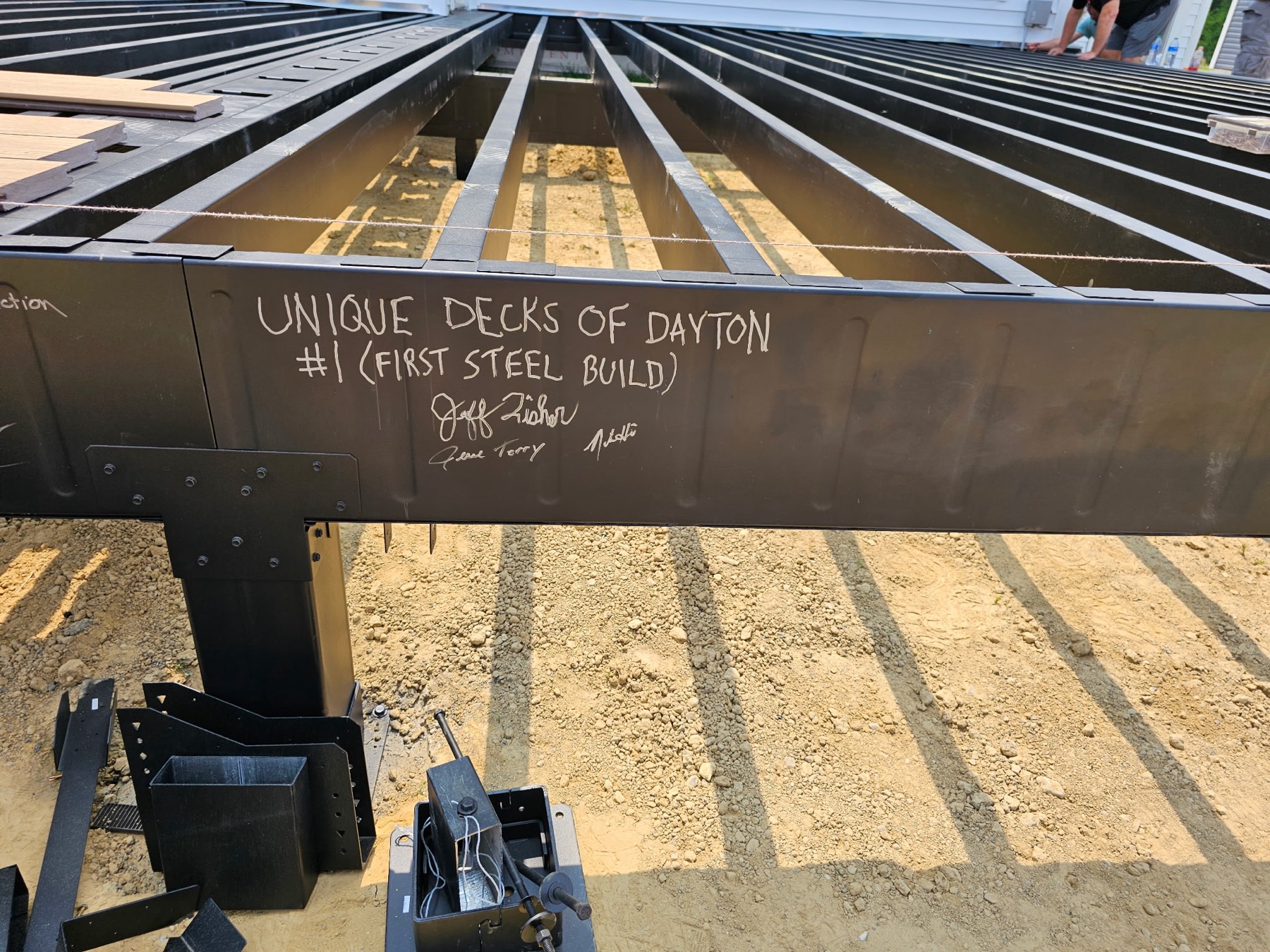 Black steel deck framing with 'Unique Decks of Dayton #1 (First Steel Build)' written on the beam and signed by the crew