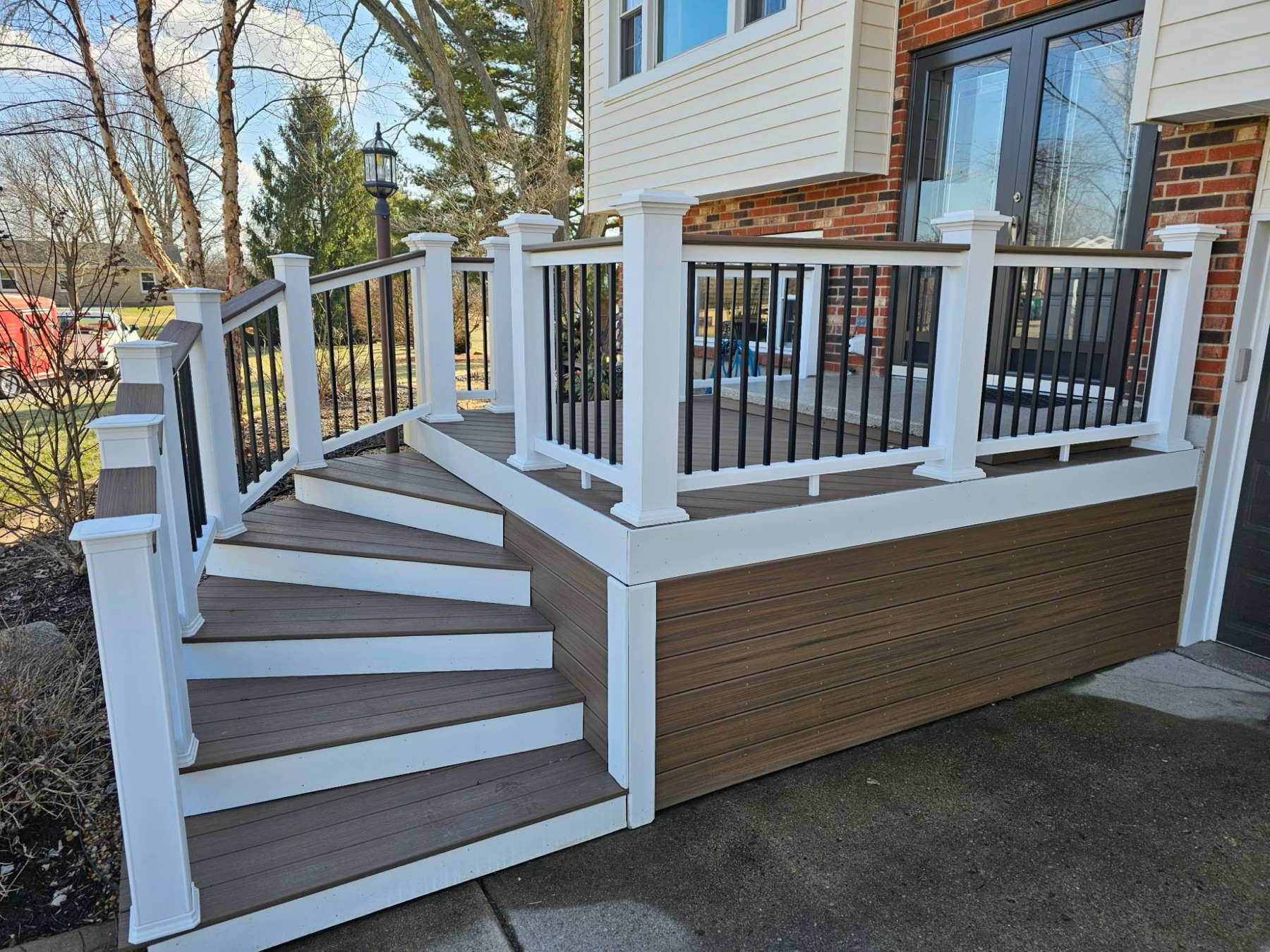 Front porch with brown composite decking, white vinyl rail posts, black balusters and a curved run of stairs